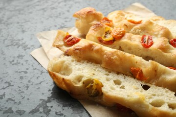 Pieces of delicious focaccia with tomatoes on gray textured table, closeup