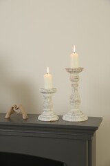 Stylish candlesticks with burning candles and other decor on fireplace near white wall indoors
