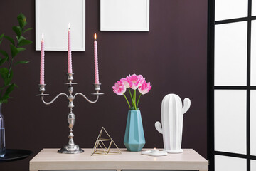 Elegant candlestick with burning candles and decor on table near brown wall