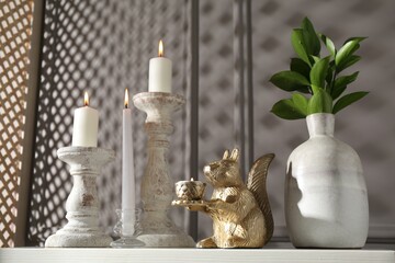 Elegant candlesticks with burning candles, branches in vase and other decor on dresser near grey...