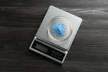 Laboratory scale with Petri dish of sample on wooden table, top view