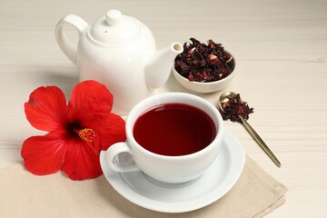 Delicious hibiscus tea in cup, teapot, dry roselle sepals and flower on light wooden table