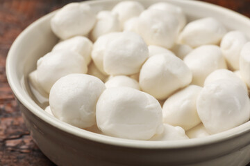 Tasty mozzarella cheese balls in bowl on wooden table, closeup