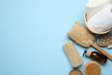 Natural loofah sponges, cosmetic product, brushes and towels on light blue background, flat lay. Space for text