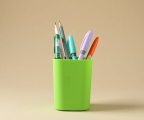 Pencils and pens in holder on beige background