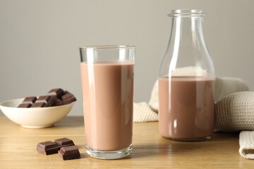 Tasty chocolate milk in glass, bottle and pieces on wooden table against grey background