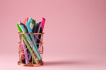 Different stationery in pen holder on pink background. Space for text