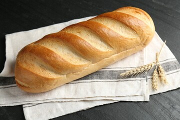 Loaf of bread and spikes on black textured table, closeup