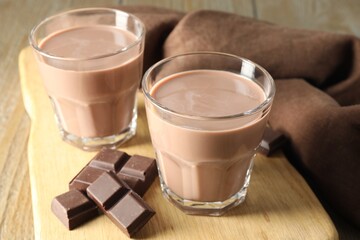 Tasty chocolate milk in glasses and pieces on table, closeup