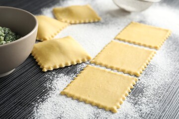 Uncooked ravioli, stuffing and flour on wooden table, closeup