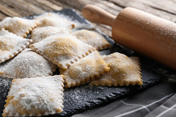 Uncooked ravioli and rolling pin on wooden table, closeup