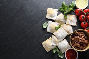 Uncooked ravioli, bolognese, sauce, tomatoes and basil on black table, flat lay. Space for text