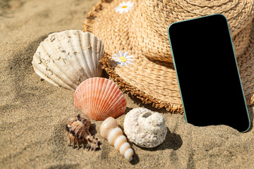 Smartphone on sand with shells and beach hat.