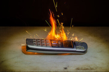A burning push-button landline phone with bright flames and sparks is a symbol of outdated technology, danger of overheating or burning electronics.