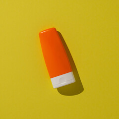 Orange square plastic bottle on a vivid yellow surface, creating a minimalistic and vibrant composition