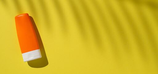 Vibrant banner orange sunscreen bottle on a bright yellow backdrop with tropical shadow overlays