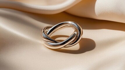 A beautifully crafted twisted ring made of silver is displayed on gentle satin fabric. The soft afternoon light highlights the intricate design and polished surface of the jewelry