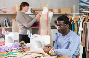 Working in sewing workshop - male tailor working at a sewing machine making stitches on fabric