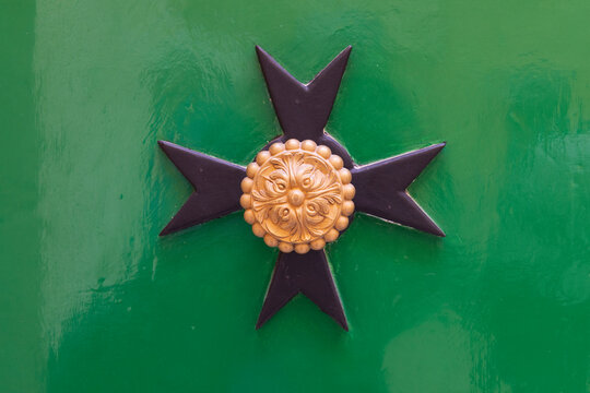 Malta, Birgu. Maltese Cross plaque on a green wall.