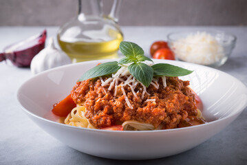 Spaghetti Bolognese in a deep dish on a marble table with ingredients around. Side view, close-up.