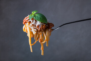 A fork with spaghetti Bolognese on a gray background close-up.