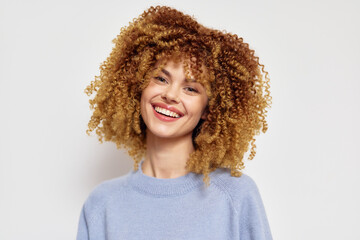 Smiling young woman with curly hair wearing a light sweater against a neutral background Her joyful expression adds warmth to the image, highlighting her personality and charm