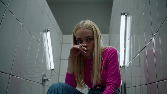 Contemplative young woman smoking in urban bathroom setting