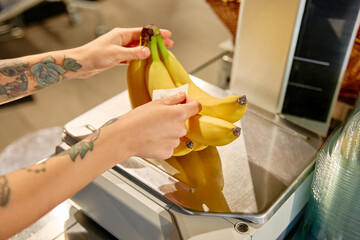 Grocery store worker weighing bananas at checkout scale