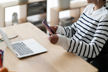A woman is taking a break from working on her laptop. She is checking her phone for messages or social media updates.