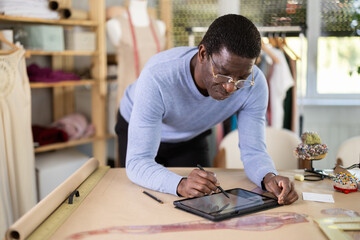 Male tailor draws sketch of future clothing on an electronic tablet. Working with modern gadgets in...