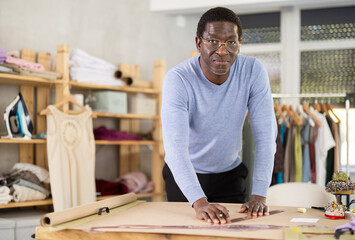 Male tailor draws sketch of future clothing on paper using patterns in a sewing workshop