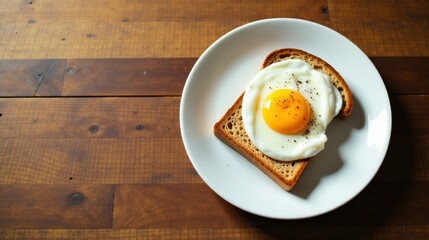 A solitary fried egg, perfectly centered atop a slice of toasted whole-grain bread, rests on a pristine white plate, elegantly presented against a backdrop of rich, warm-toned wood.