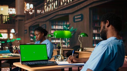 African american male nurse studies anatomy textbooks next to green screen in a university library, using academic database for a successful medical career. Med school. Camera A.
