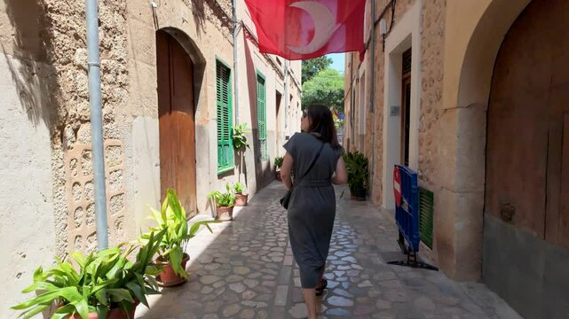 Woman strolling down a narrow cobblestone street in soller, mallorca, enjoying the charming architecture and sunny weather