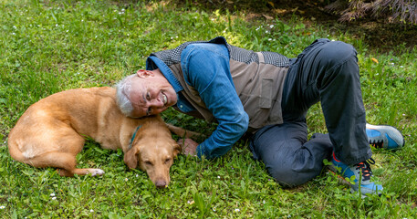 middle aged man lying in the grass of a park enjoying happy moments with his dog