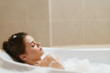 Naklejka premium Relaxed young woman enjoying a soothing bubble bath, closed eyes and serene expression, creating a calming atmosphere for self-care and wellness.