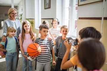 boy take a photo of classmates with teacher in hallway