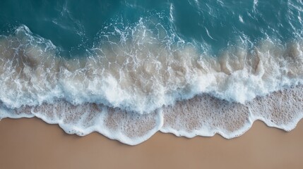 Fototapeta premium Aerial view of gentle ocean waves rolling onto a sandy beach, creating foamy patterns along the shoreline