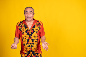 Surprised senior man shrugging against yellow background