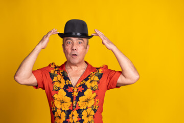 Surprised senior man touching his black hat on yellow background
