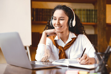 Doing Homework. Portrait of smiling young woman sitting at desk with pen, writing and taking notes...