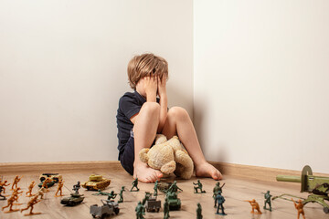 The child huddled in a corner with a teddy bear and was afraid of a toy soldiers. The child, as the...