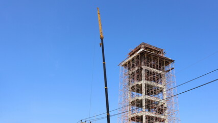 Tower under construction. Concrete tower under construction with scaffolding and crane on blue sky background with copy space. selective focus