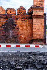 Generated imageHistoric red brick wall of Chiang Mai's Tha Phae Gate, Thailand, with a street under repair in the foreground, showing signs of demolition.