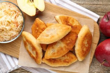 Delicious fried pyrizhky (stuffed pies) and apples on wooden table, flat lay