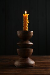 Burning candle in candlestick on wooden table