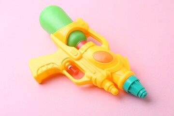 Bright plastic water gun on light pink background, closeup
