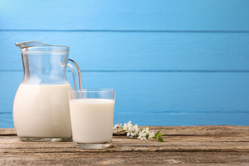 Fresh milk and blossoms on wooden table against light blue background. Space for text