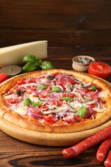 Tasty pizza with smoked sausages and ingredients on wooden table, closeup