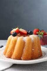 Tasty Bundt cake with powdered sugar and berries on light grey table, closeup. Space for text